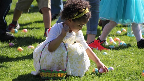 Young-girl-wearing-white-dress-bends-down-to-collect-an-egg-for-her-basket.jpg