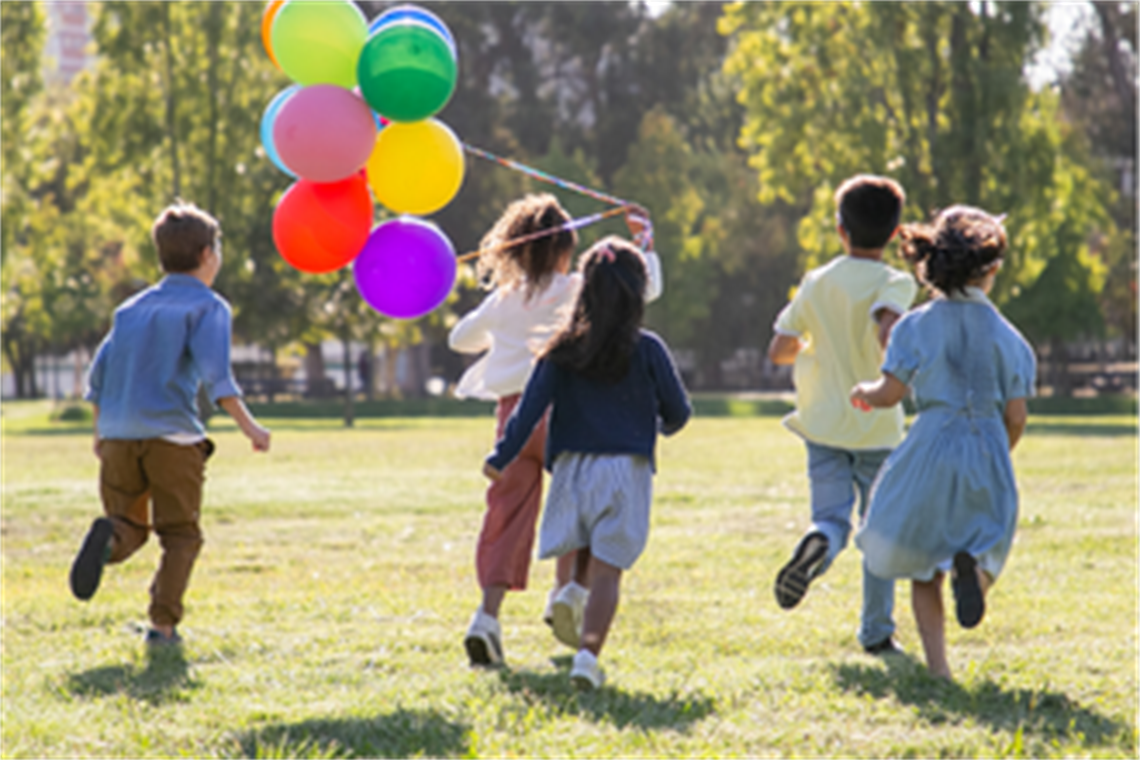 Image of children running across a grass field with a bunch of balloons