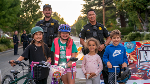 Menlo Park police officers with children on bikes and scooters at National Night Out