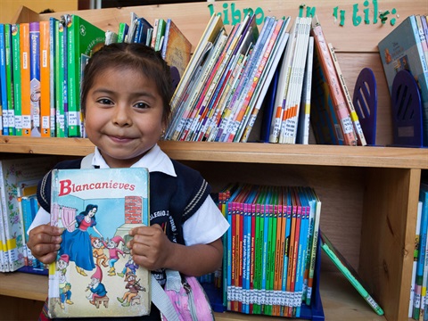OpenCities--young-hispanic-girl-holds-spanish-language-childrens-book-in-front-of-library-book-shelves.jpg