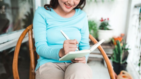 woman-writes-in-a-notebook-while-sitting-on-a-patio.jpg