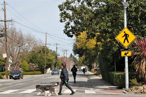 Pedestrian crosses Middle Ave at Blake Street and people scooter, bike, and drive along Middle